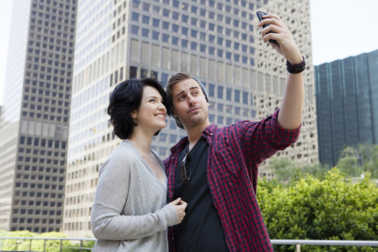 Caucasian couple taking selfie with cell phone in city