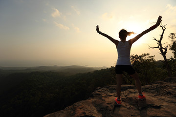 silhouette of young successful woman open arms on sunset mountain peak