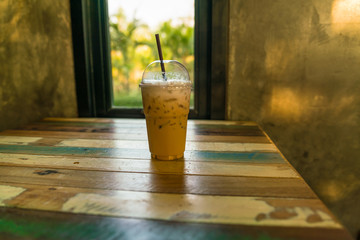 capuchino Ice coffee in plastic cup with straw on wooden table and window at day light - copy space

