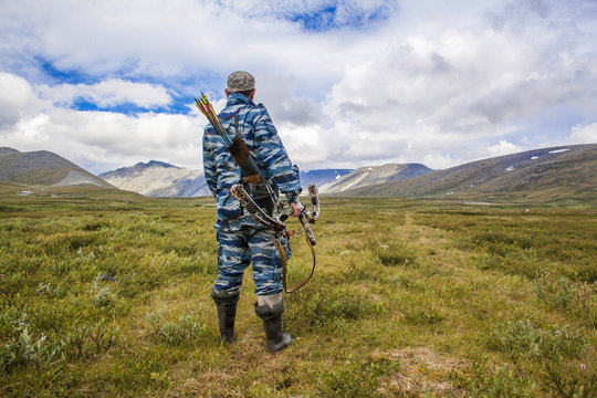Mari hunter carrying crossbow in remote field - Powered by Adobe