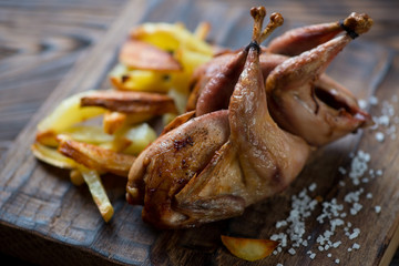 Whole baked quails with potato wedges, close-up, selective focus