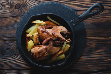 Above view of a frying pan with baked quails and potato