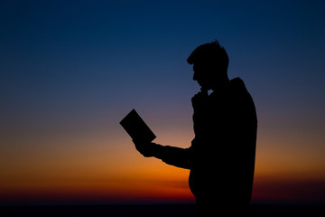 Man reading in the field against sunset