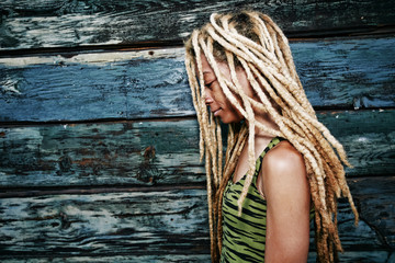 Woman with blonde dreadlocks at wooden wall