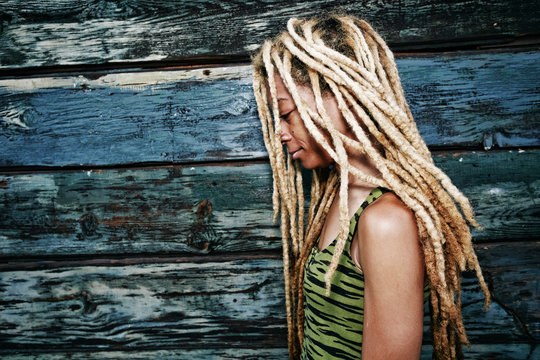 Woman with blonde dreadlocks at wooden wall