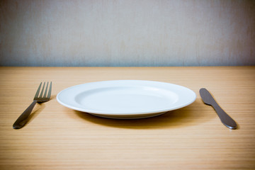 Empty plate with fork and knife on wooden table. Table arrangement. Vintage effect style picture