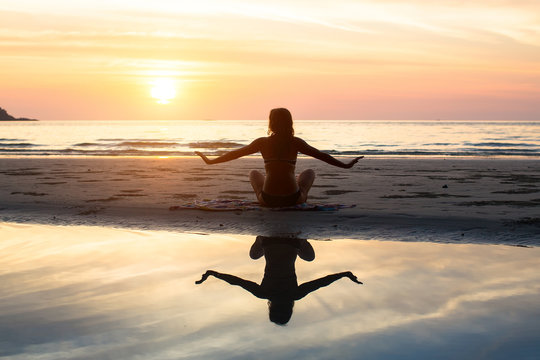 Silhouette yoga woman on the background of the sea and amazing sunset. Healthy lifestyle.