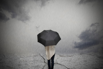 Depressive Frau steht mit Regenschirm unter einem wolkenverhangen Himmel