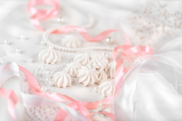 Obraz na płótnie Canvas French meringue cookies for wedding background with pearls, pink and white satin ribbons and lace, close-up