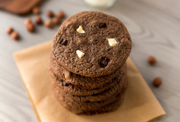 Chocolate cookies with hazelnuts, white chocolate and dark chocolate on parchment, wooden background, close-up