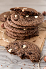 Chocolate cookies with hazelnuts, white chocolate and dark chocolate on parchment, wooden background, vertical, close-up