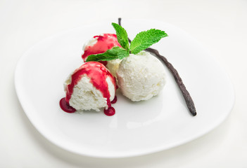Three scoops of vanilla ice cream with strawberry syrup and mint on a white plate and a vanilla bean, white background