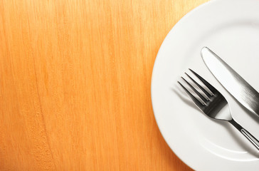 Photo of the fork and knife with white plate on wood