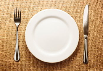 Photo of the fork and knife with white plate on sacking