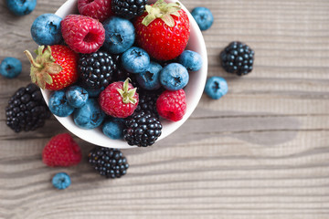 Mix of fresh berries in a basket on rustic wooden background. Close up, top view, high resolution product. Harvest Concept