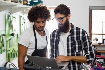 Mechanic with colleague using laptop at workshop