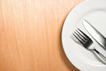 fork and knife with white plate on wooden background