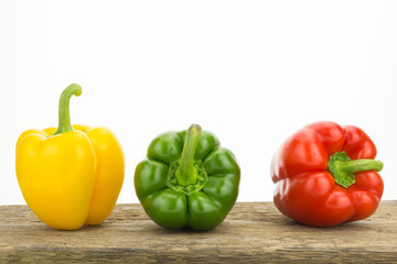 Yellow, green and red bell peppers on wooden surface, on white background with copy-space