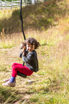 Young girl riding a zip-line, grassy playground warm summers day. 