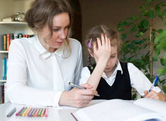 Mother helping her tired daughter with homework at home.