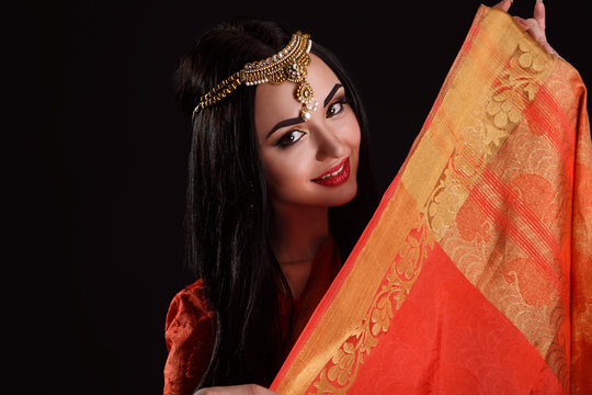 Beautiful Young Indian Woman in red Traditional Clothing with perfect Makeup and Oriental Jewelry.