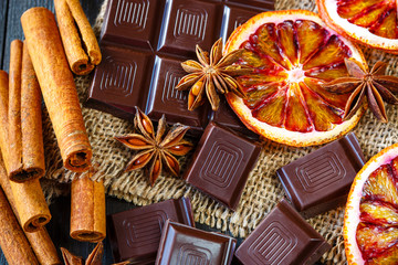 Dark chocolates with dry oranges, cinnamon and anise on burlap on rustic table