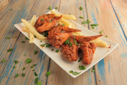 Buffalo wings with french fries on a plate on wooden background
