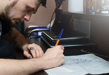 Artist encircles pen sketch of a tattoo on the desktop.