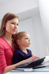 Young busy mum working at the table with her little child. Concept of family business and occupation.