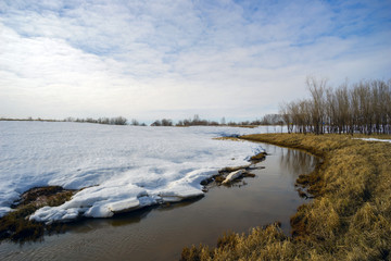 Spring landscape with a brook behind  snow mound .