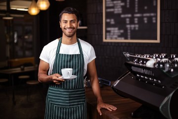 Smiling barista holding a cup of coffee - obrazy, fototapety, plakaty