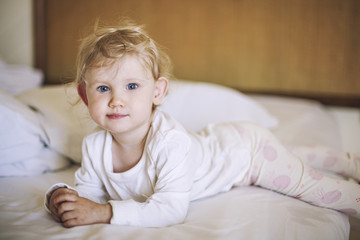 Naklejka premium Small child lies in the bedroom on the bed and smiling