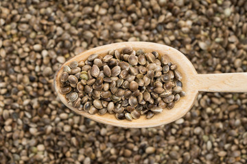 Wooden spoon with hemp seeds coming from right seen from above over a hemp seed background