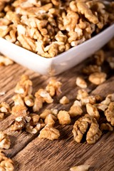 Several walnuts spilled around white bowl on wooden board