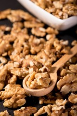 Spilled walnuts on black slate stone and wooden spoon