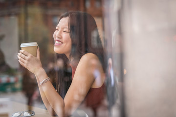 young chinese woman sitting next to windows in cafe.