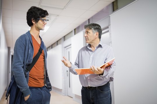 Professor With Notebook Talking To A Student