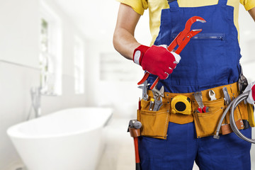 plumber with tool belt standing in bathroom - obrazy, fototapety, plakaty