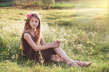 Girl with peony in her hair sitting on the field and looking int