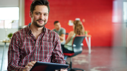Confident male designer working on a digital tablet in red creative office space