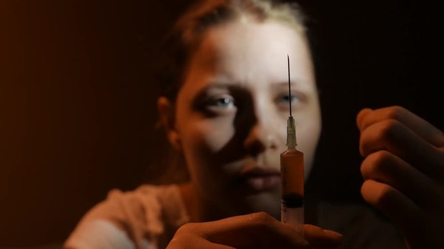 Addicted junkie teen girl with a syringe sitting and thinking about something. Focus on a syringe. Close up. 4K UHD