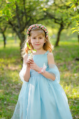 Little girl in blue dress under the blooming tree in spring garden