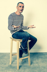 expressive body language - smiling young man with short hair talking with his flat hands sitting alone on a stool, green effects