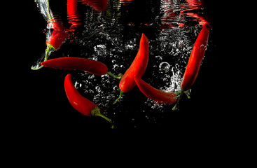 Obrazy na Szkle  Kilka czerwonych papryczek wpadło do wody na białym tle na czarnym tle