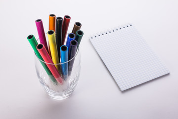 felt-tip pens in a glass and a notebook on a white background