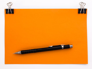 orange piece of paper with black paper clips and pencil