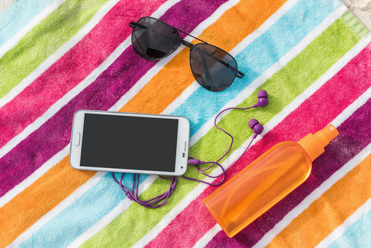 Summer vacation beach accessories - smartphone, sunglasses, sunscreen. Travel packing essential must-have items to bring on a holiday trip to the Caribbean. Tech phone with music app and earphones.