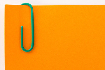 green paper clip on an orange sheet of paper macro