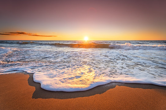 Colorful ocean beach sunrise with deep blue sky and sun rays.