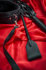 Riding crop, a whip flogger, leather choker and leash on red satin, kinky sex toys for dom / sub...